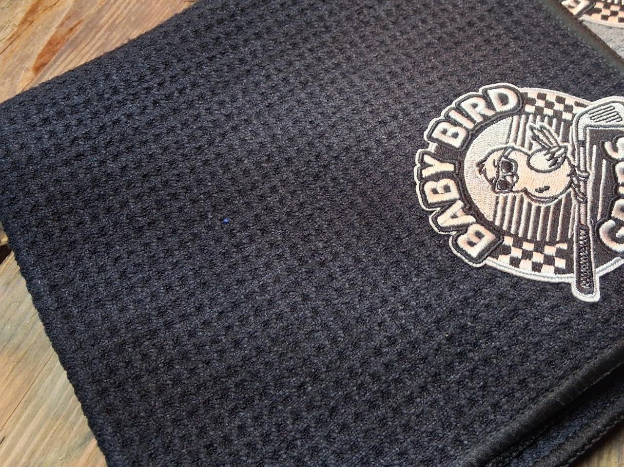 A black waffle golf towel with a gray Baby Bird Grips patch