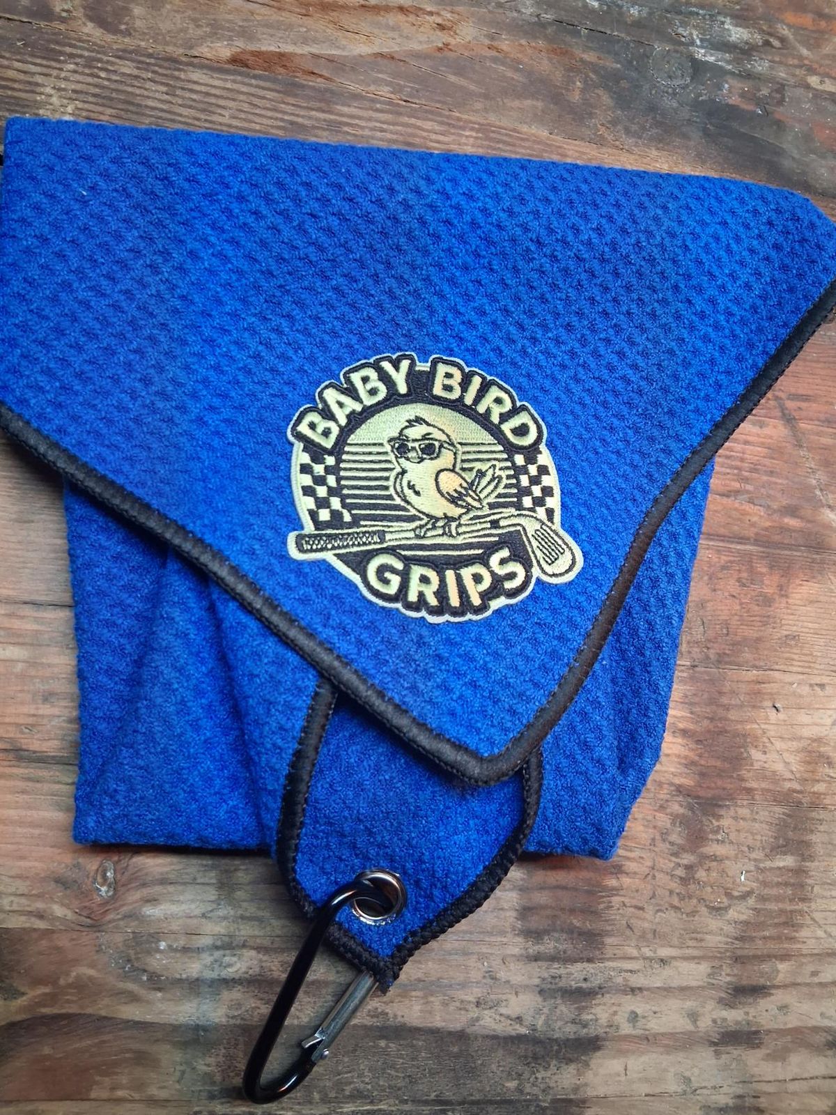A blue waffle golf towel with a green Baby Bird Grips patch and a carabiner